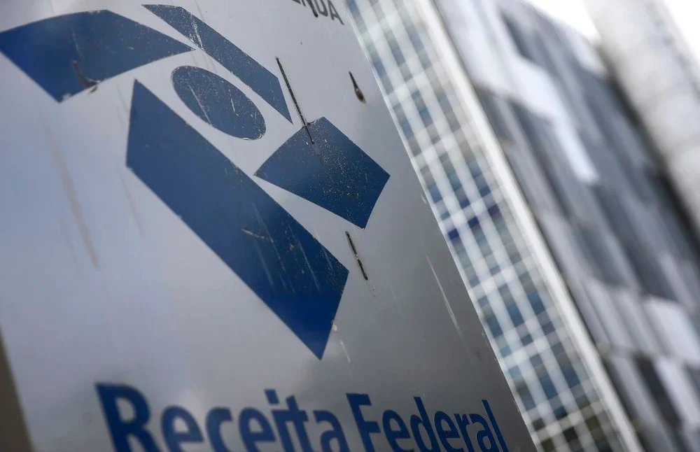 Logotipo da Receita Federal em tela de computador ao lado de calculadora e documentos fiscais