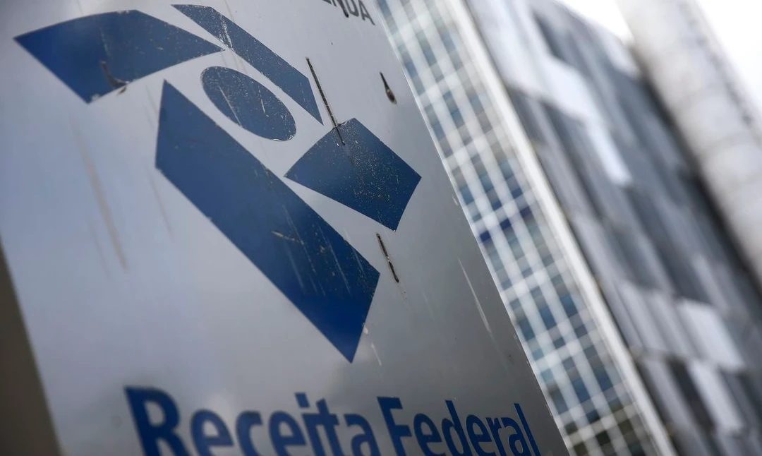 Logotipo da Receita Federal em tela de computador ao lado de calculadora e documentos fiscais