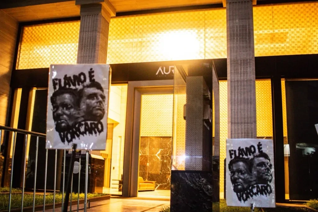 Placas com os rostos de Flávio Bolsonaro e Daniel Vorcaro e a frase Flávio é Vorcaro em frente ao antigo prédio do Banco Master na Faria Lima
