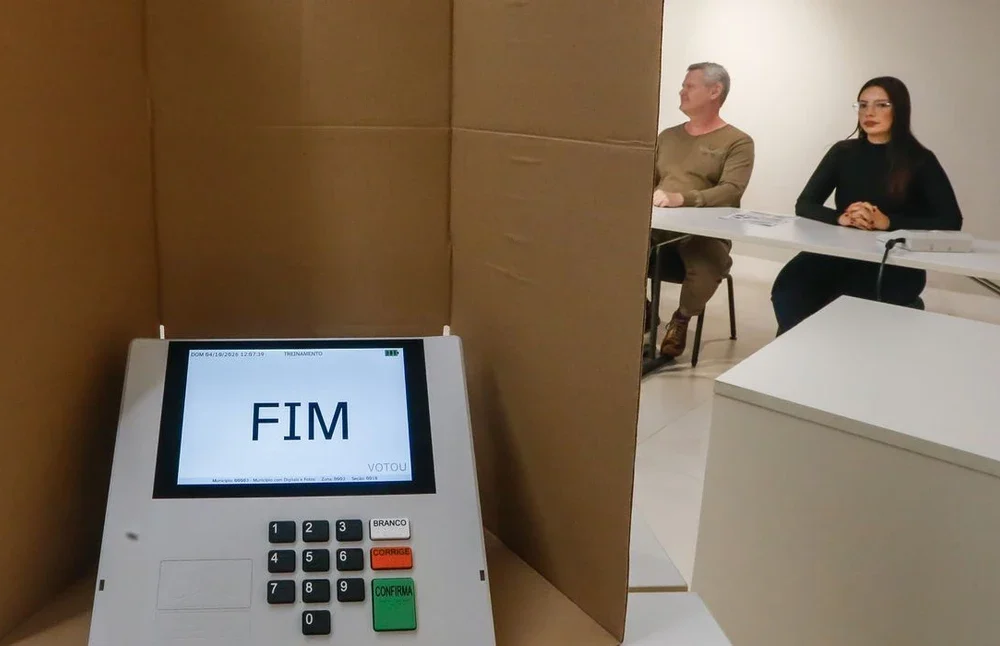 Eleitor entregando celular à mesa receptora antes de entrar na cabine de votação