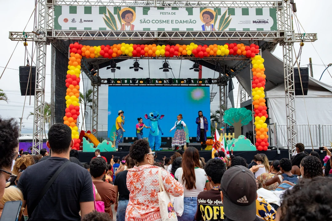 Crianças e famílias comemorando São Cosme e Damião na quadra da União de Maricá, com apresentações de escolas de samba mirins e distribuição de doces