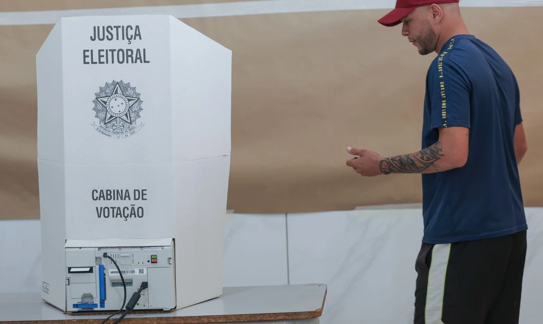 Papel com números de candidatos e caneta ao lado, ilustrando a colinha usada na urna eletrônica