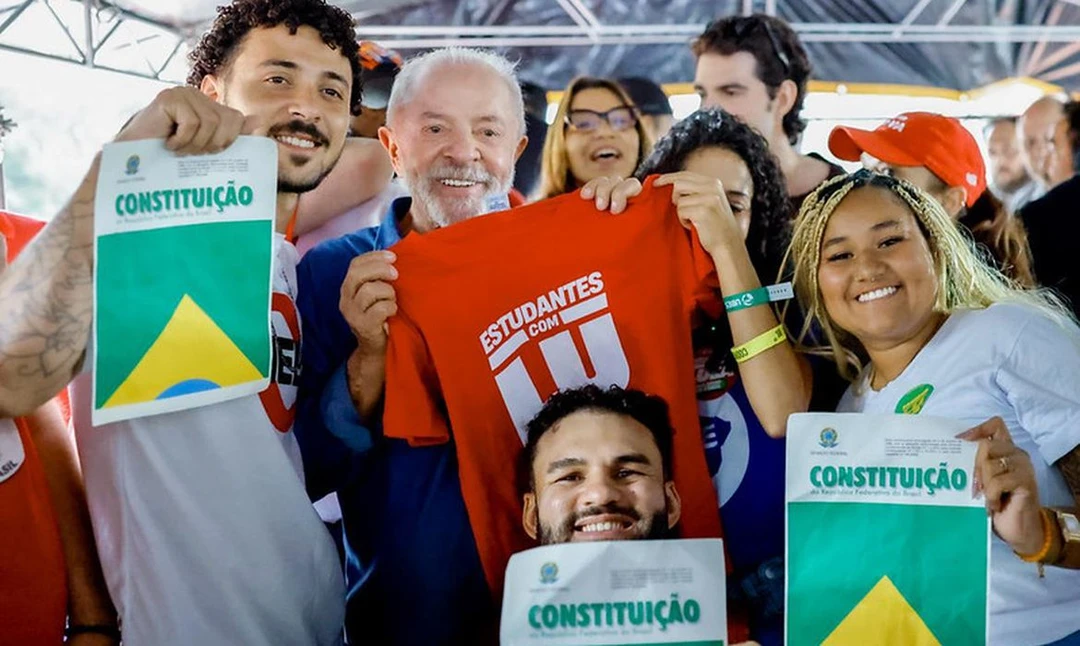 Lula em vídeo selfie rodeado por jovens ao fundo, anunciando o programa universitário Pé de Meia