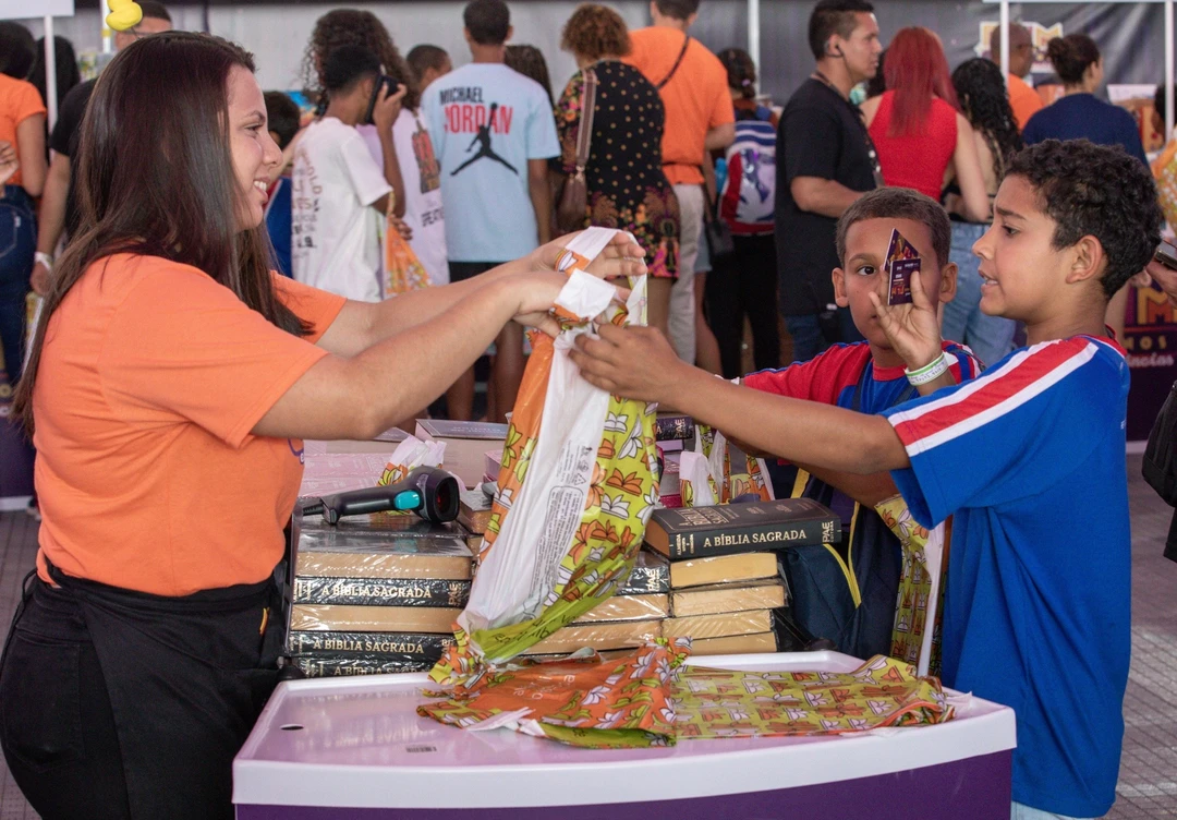 Cartão magnético com vale‑livro de R$300 sendo entregue a professor durante a FLIM 2026 em Maricá